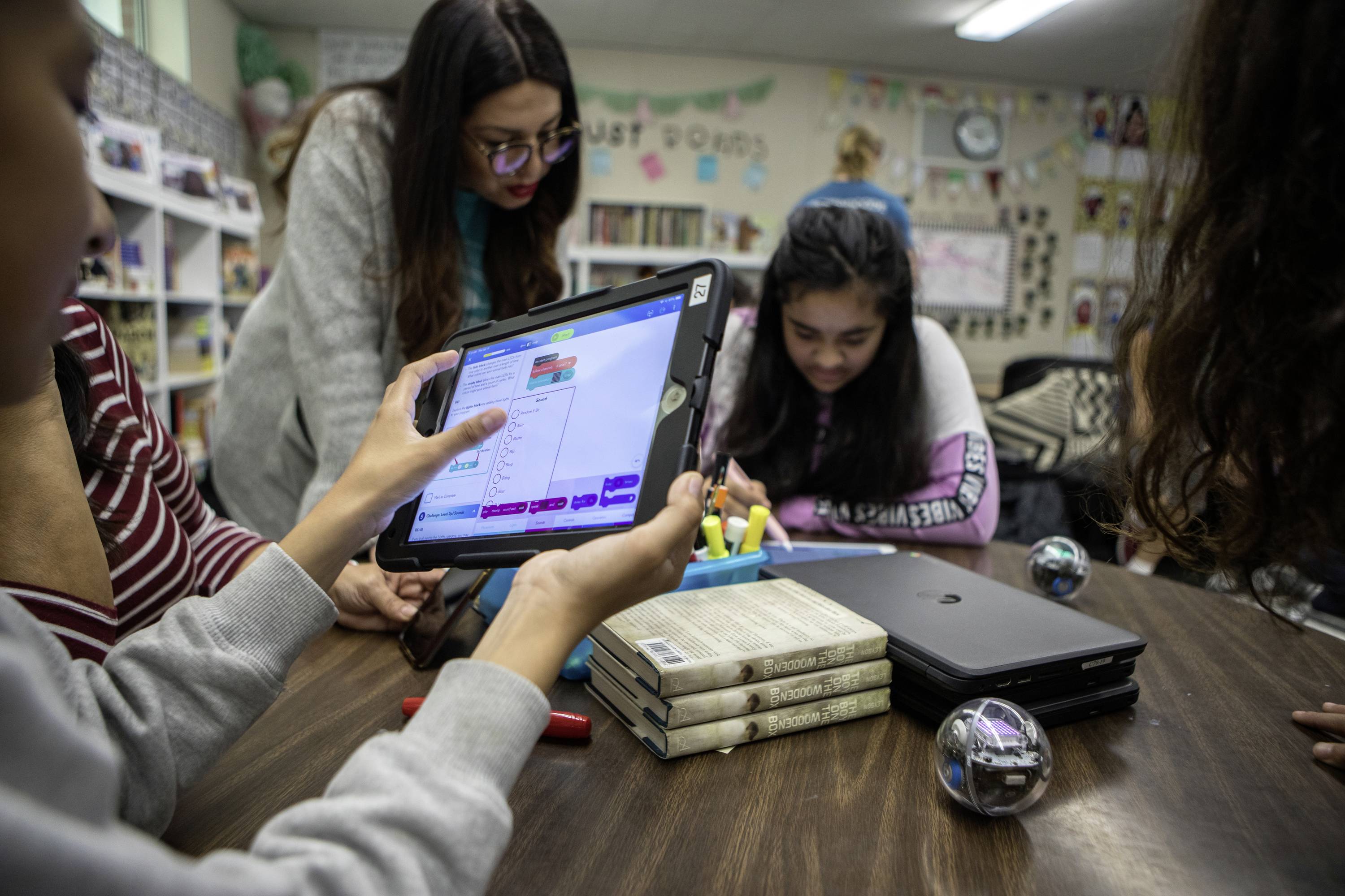 Eine Gruppe Schüler programmiert Roboter mit Tablets in einem Klassenzimmer. Das Hauptaugenmerk liegt auf einem Tablet mit Code.