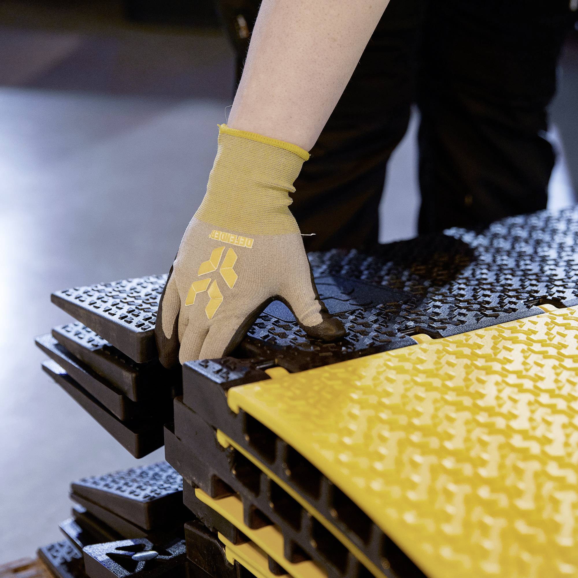 Eine Person mit Arbeitshandschuhen stapelt gelbe Bodenplatten.