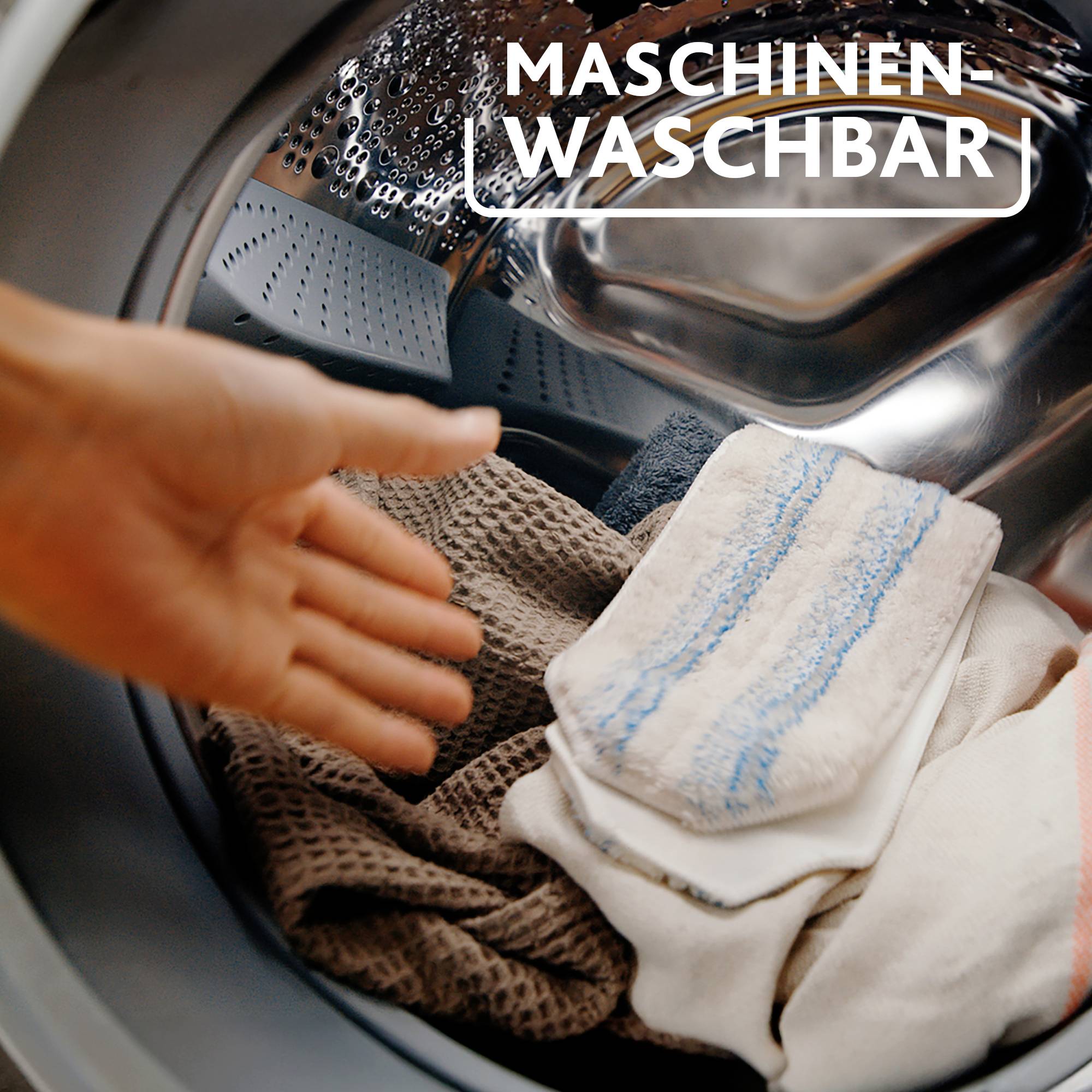 Hand legt weiße und beige Tücher in eine geöffnete Waschmaschine. Darüber steht 'MASCHINEN WASCHBAR'.