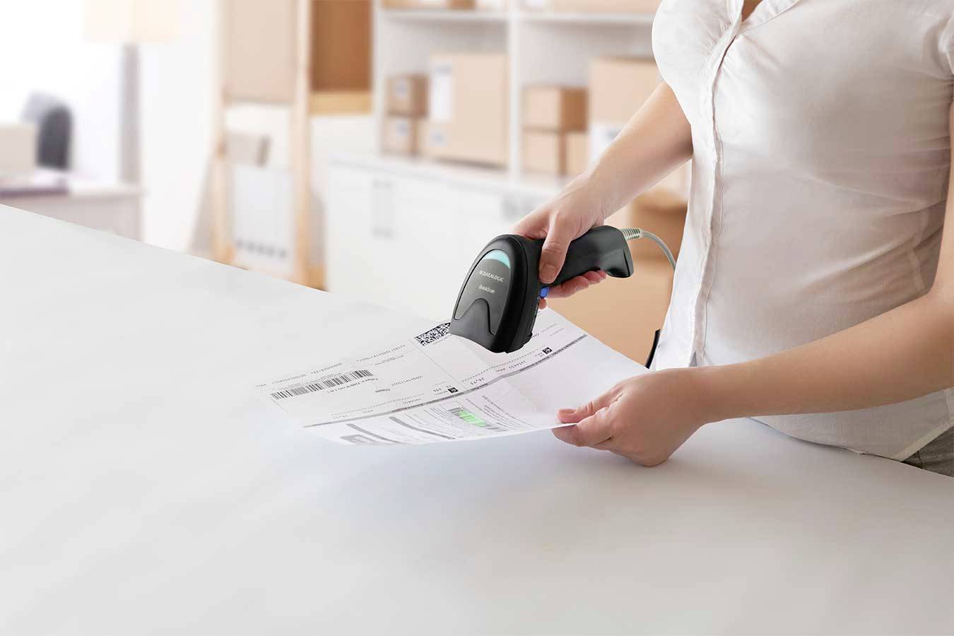 Eine Person scannt ein Barcode auf einem Dokument in einem Büro mit Kartons im Hintergrund.