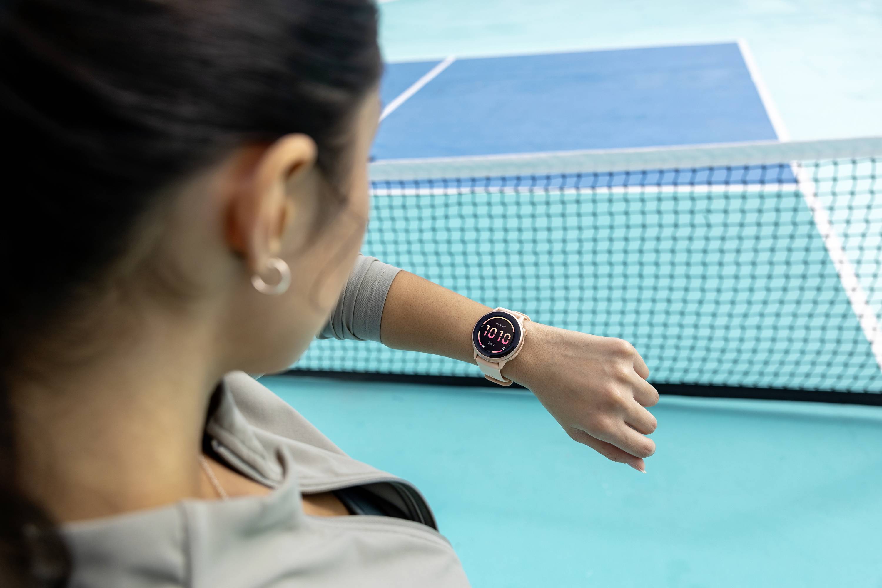 Eine Frau auf einem Tennisplatz schaut auf eine Smartwatch an ihrem Handgelenk, die 10:19 Uhr anzeigt.