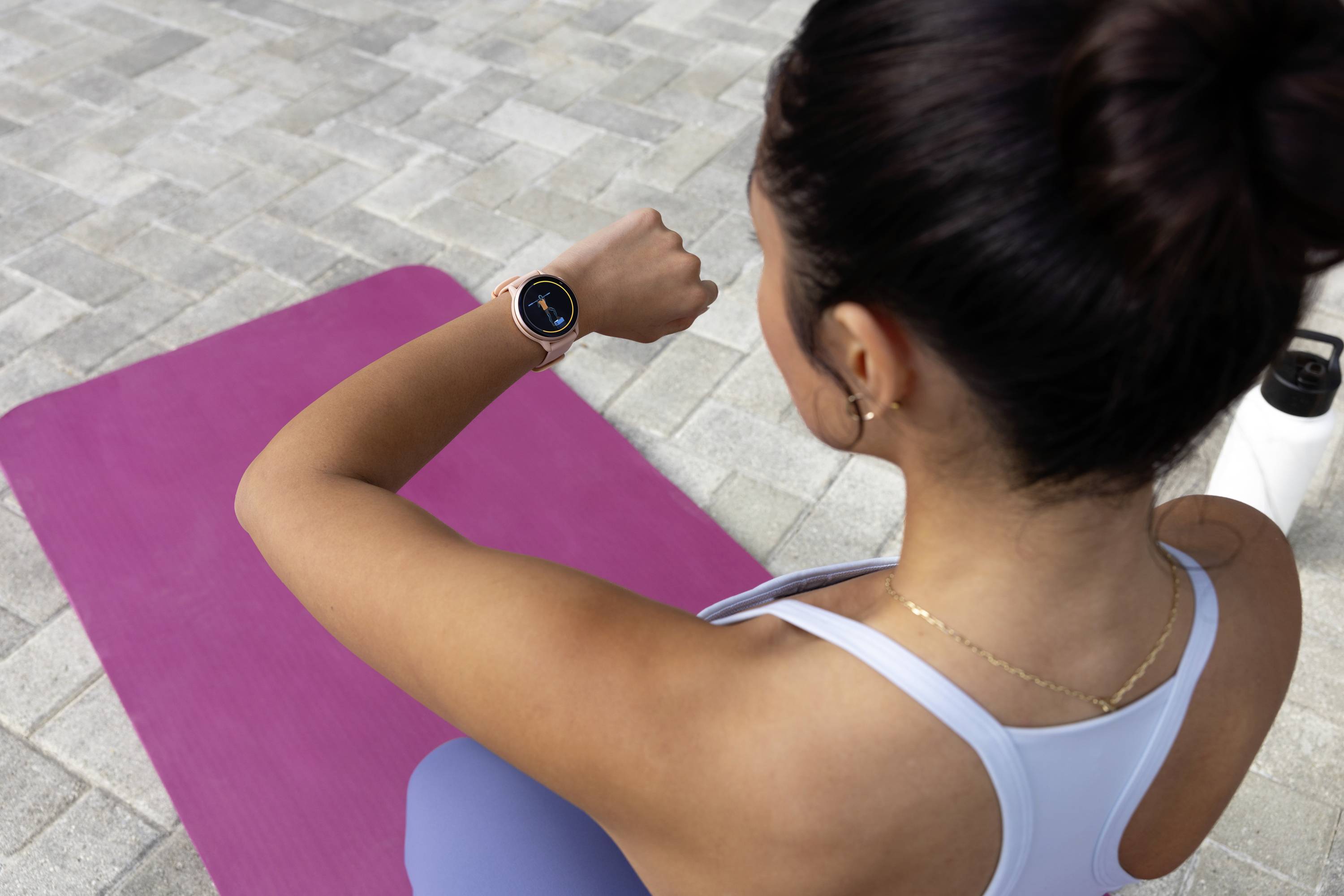 Eine Frau in Sportkleidung überprüft die Zeit auf ihrer Smartwatch, während sie auf einer lilafarbenen Yogamatte sitzt.