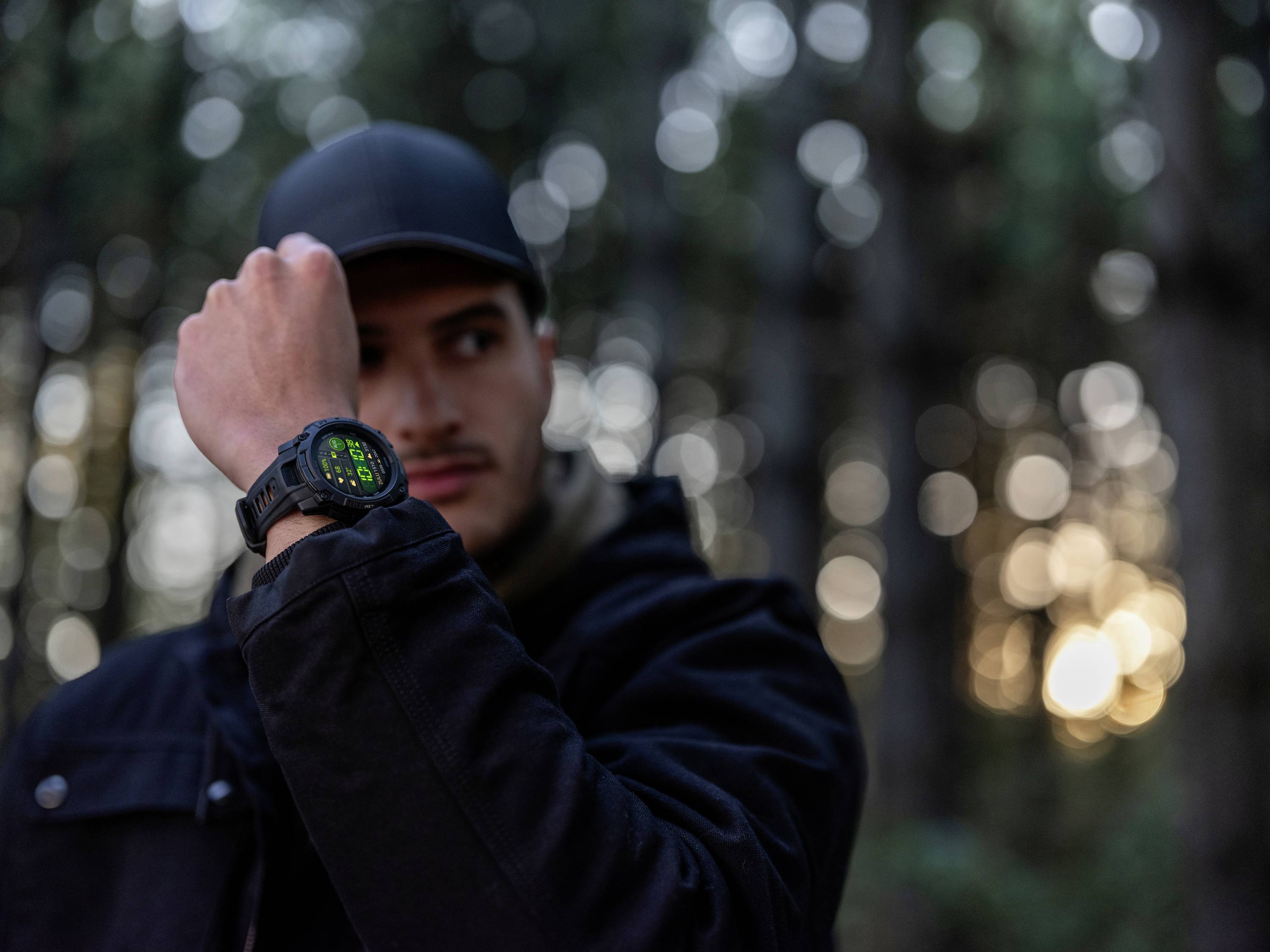 Ein Mann im Wald schaut auf seine Armbanduhr. Die Szene ereignet sich bei Dämmerung, die Bäume sind unscharf im Hintergrund zu sehen.