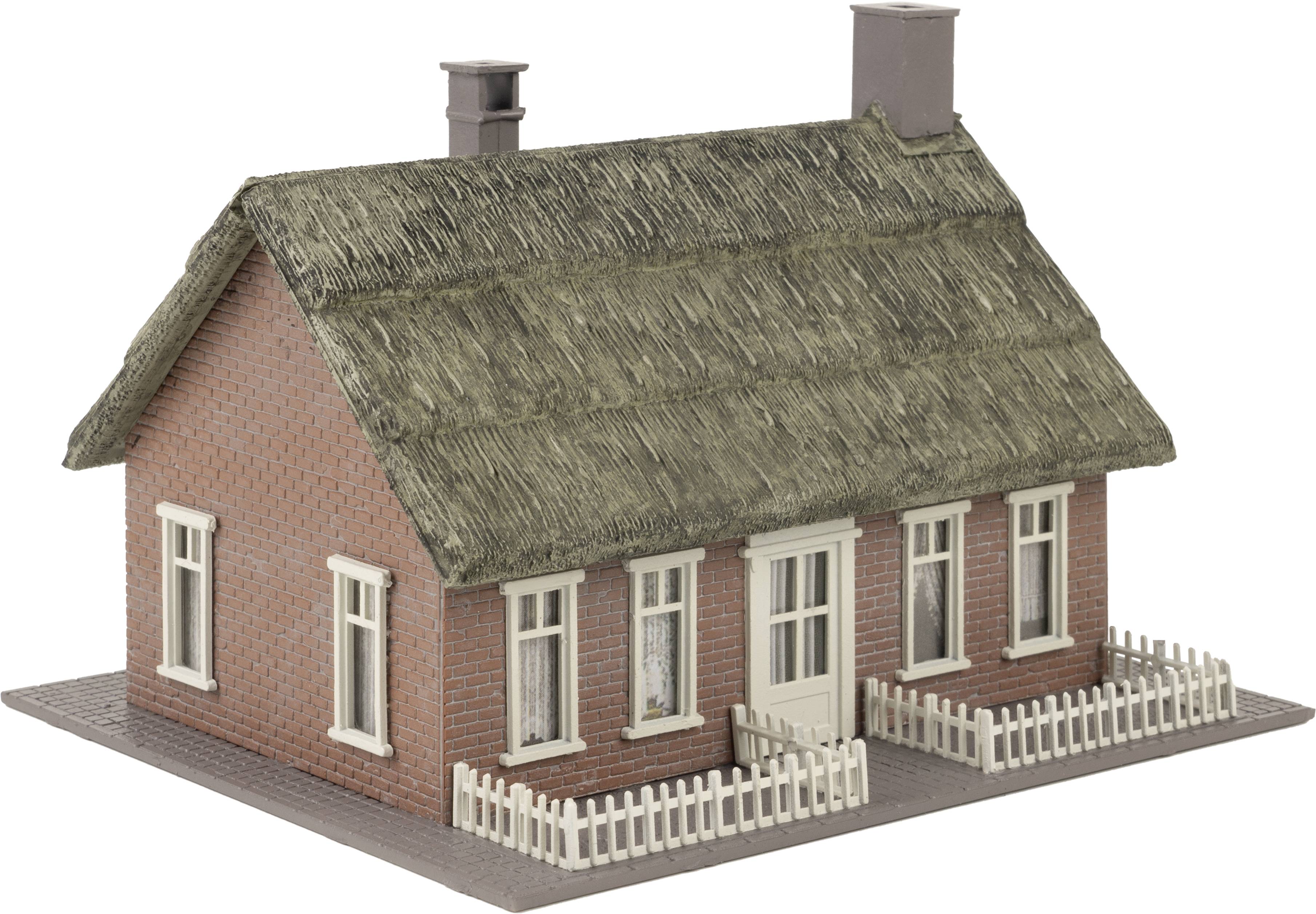 Ein kleines rotes Backsteinhaus mit Reetdach, weißen Fenstern und Türen auf einer Modellbauplatte.