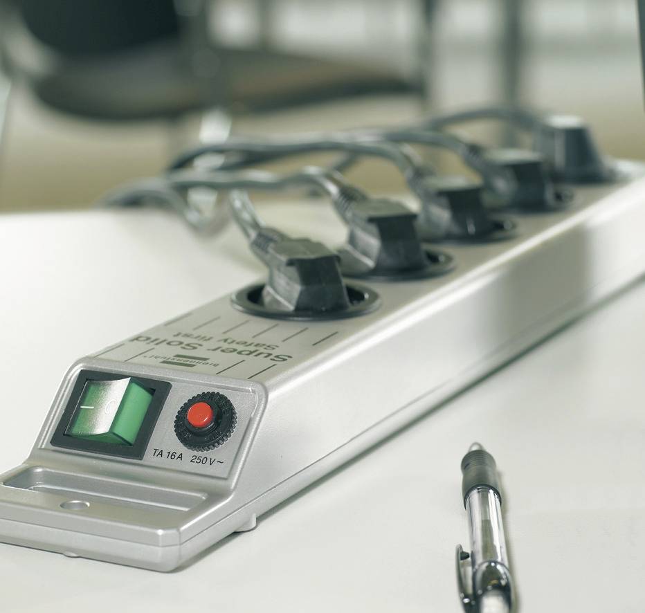 Eine Steckdosenleiste mit fünf eingesteckten Kabeln liegt auf einem Tisch. Ein Stift liegt daneben.