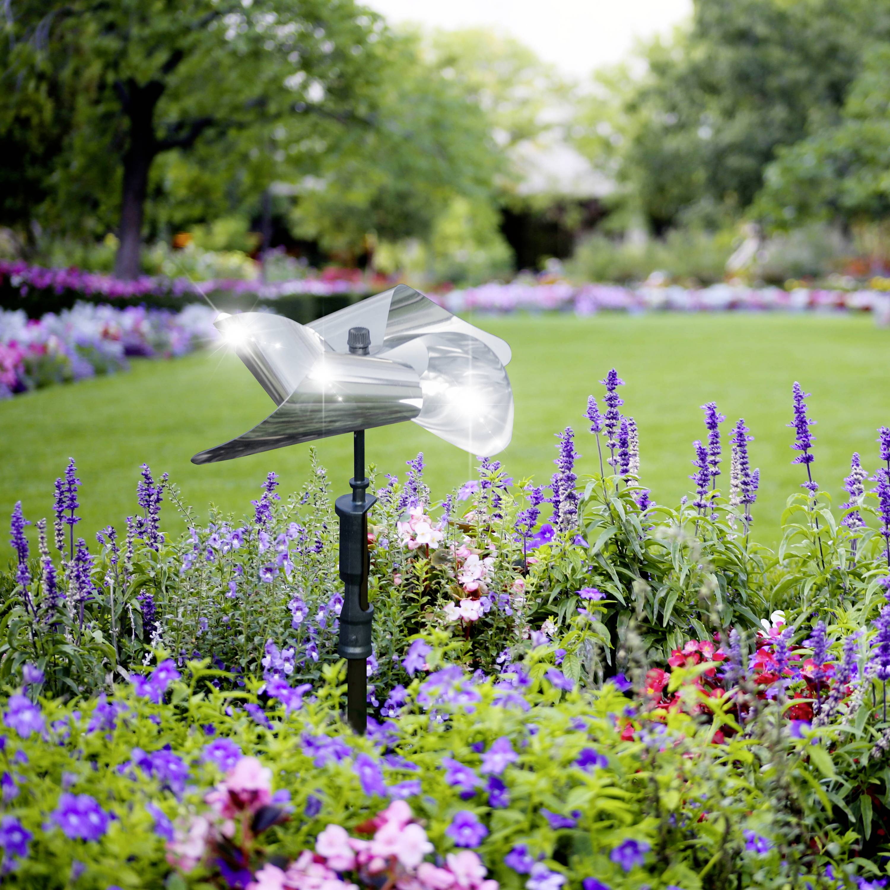 Eine automatisierte Sprinkleranlage bewässert einen Garten mit bunten Blumen, darunter große grüne Rasenflächen und verschiedene Pflanzenarten.
