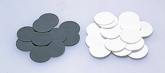 'Zwei Stapel runder Schleifpads, links schwarze und rechts weiße, auf einer grauen Oberfläche liegend.'