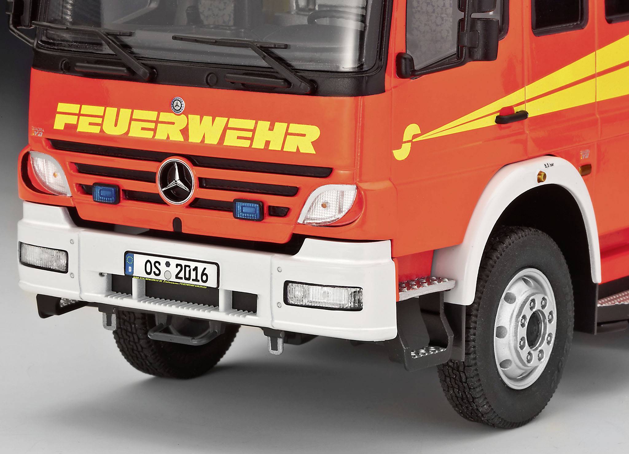 Nahaufnahme eines roten Feuerwehrautos mit der Aufschrift 'FEUERWEHR' über dem Kühlergrill. Das Fahrzeug hat ein Mercedes-Logo.