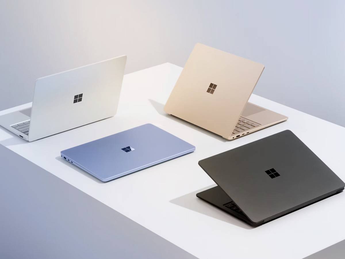 Vier farbenfrohe Laptops auf einem weißen Tisch, jeweils unterschiedlich ausgerichtet, präsentieren die vielfältige Produktpalette einer Technologiemarke in einem minimalistischen Ambiente.