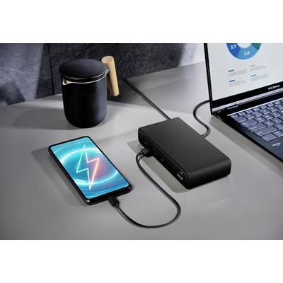 Ein Smartphone zeigt ein Ladesymbol, während es mit einer Powerbank auf einem Schreibtisch verbunden ist, neben einem Laptop und einer schwarzen Tasse.