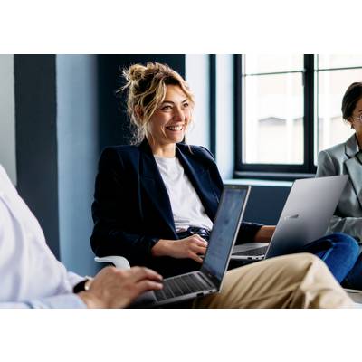 Eine lächelnde Person sitzt in einem modernen Büro mit Laptops und ist in eine kollaborative Arbeitsumgebung eingebunden.