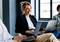 Eine lächelnde Person sitzt in einem modernen Büro mit Laptops und ist in eine kollaborative Arbeitsumgebung eingebunden.