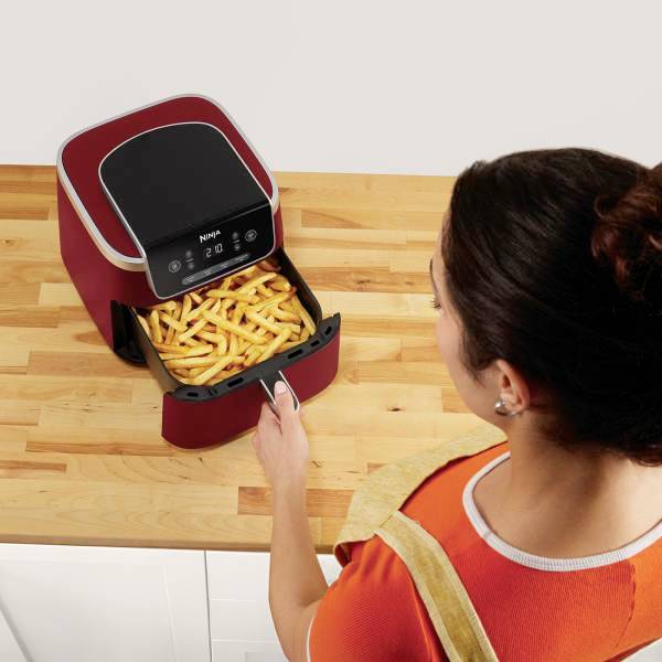 Person bereitet Pommes frites in einer roten Heißluftfritteuse auf einer Holzarbeitsplatte zu.