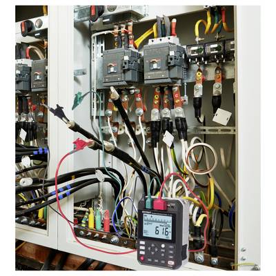 Ein elektrisches Schaltfeld mit mehreren farbigen Kabeln wird mit einem digitalen Multimeter getestet, das einen Messwert von „6,16" anzeigt.
