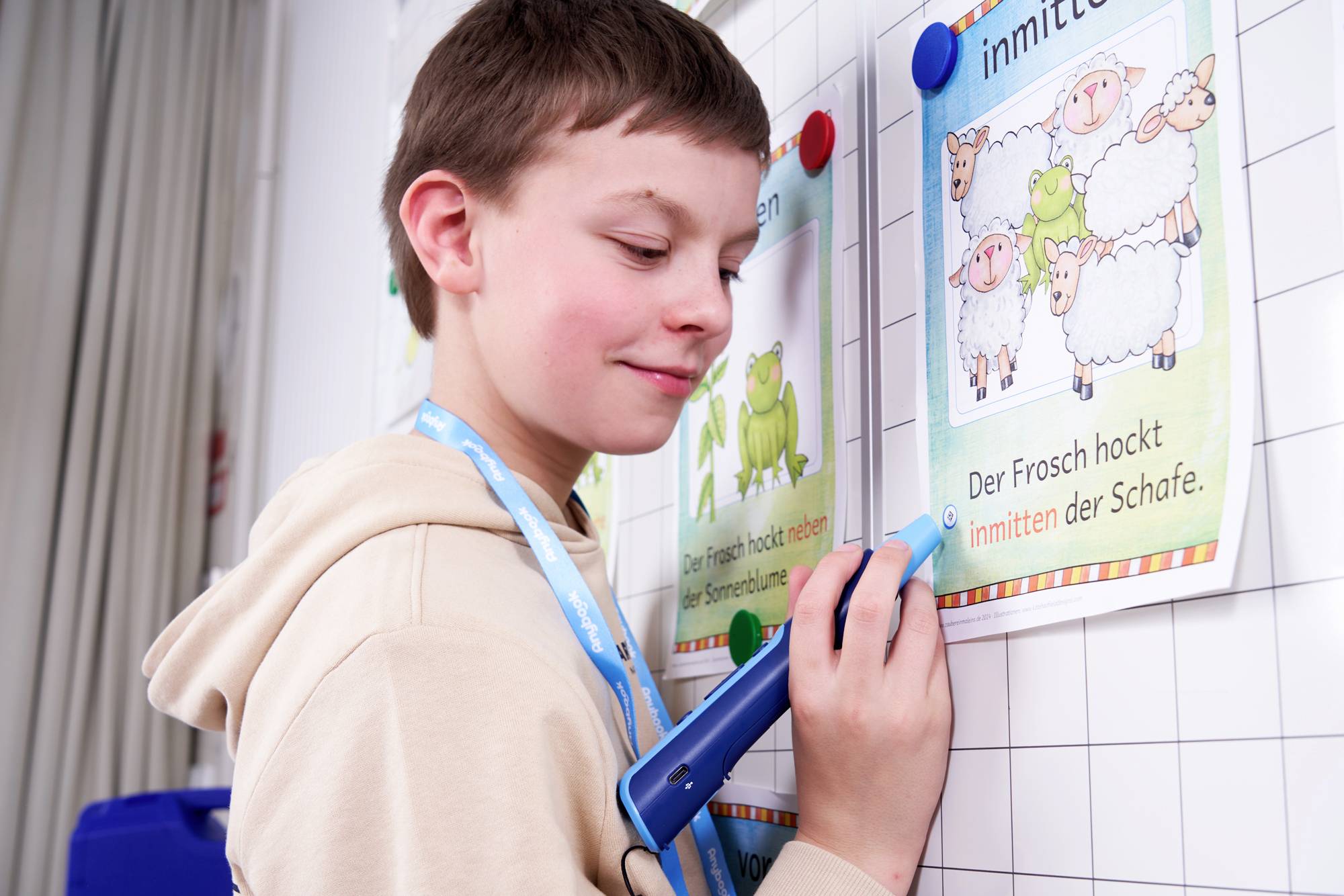 Ein Junge verwendet einen elektronischen Stift auf einer illustrierten Tafel mit Tierbildern und Text. Er konzentriert sich auf seine Aufgabe.