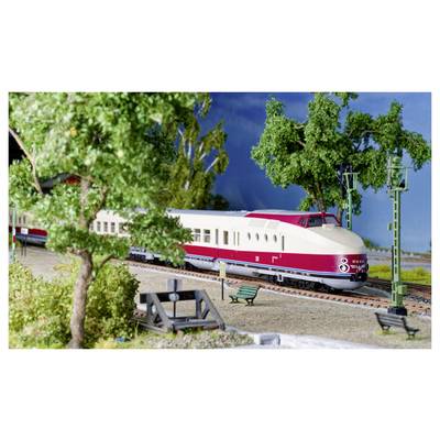 Ein roter und weißer Modellzug fährt durch eine detaillierte Landschaft mit Bäumen, Bänken und einem kleinen Bahnsteig.