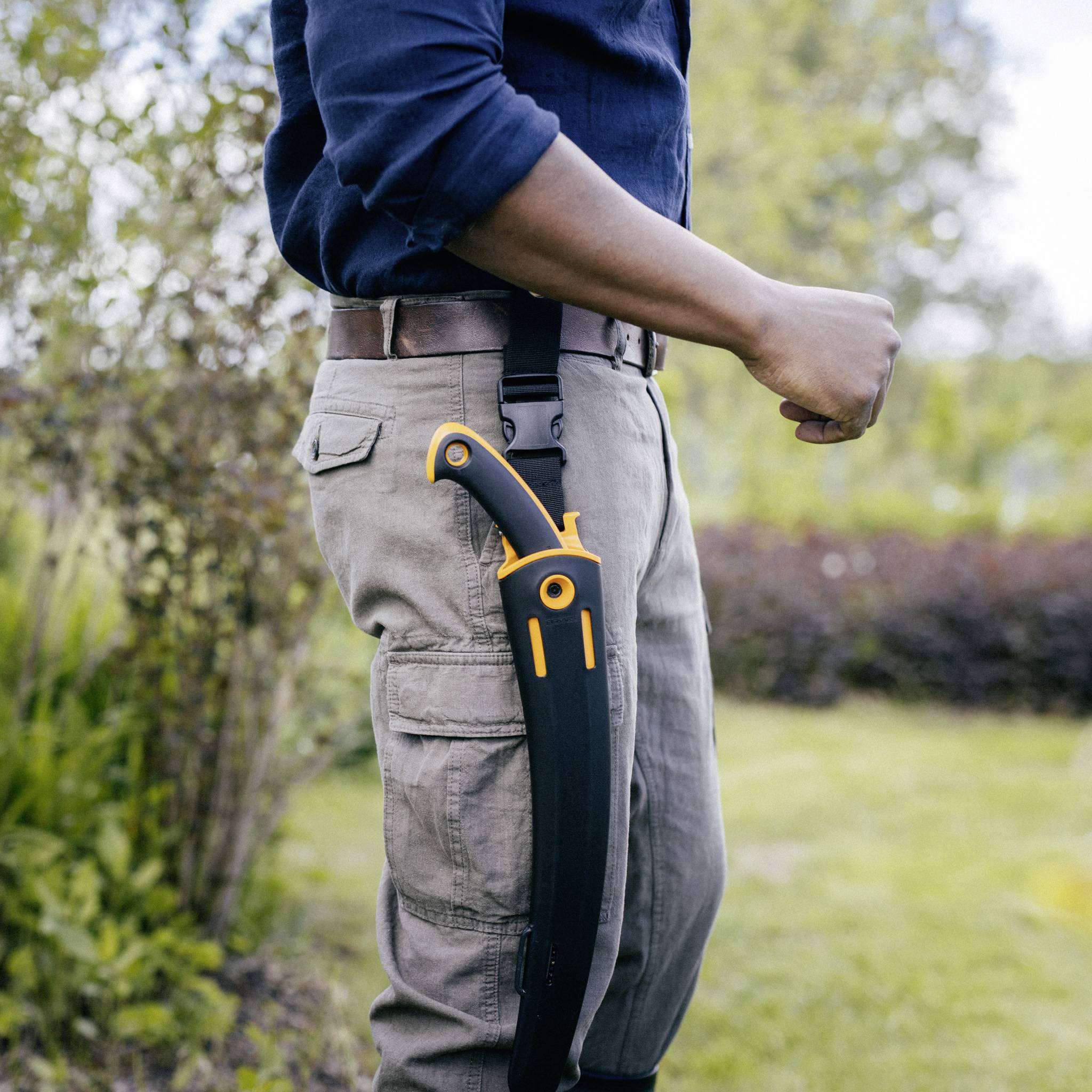 Eine Person steht im Profil im Freien und trägt ein großes, gebogenes Messer in einer Schutzhülle an der Hose befestigt.