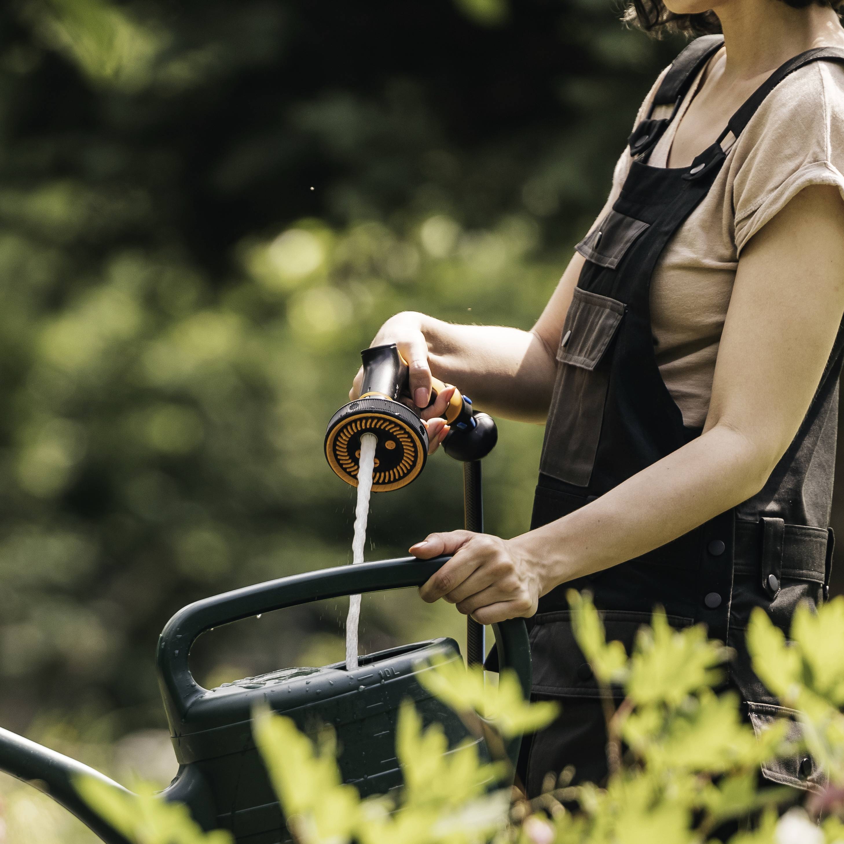 Eine Person gießt Pflanzen mit einer grünen Gießkanne im Garten. 