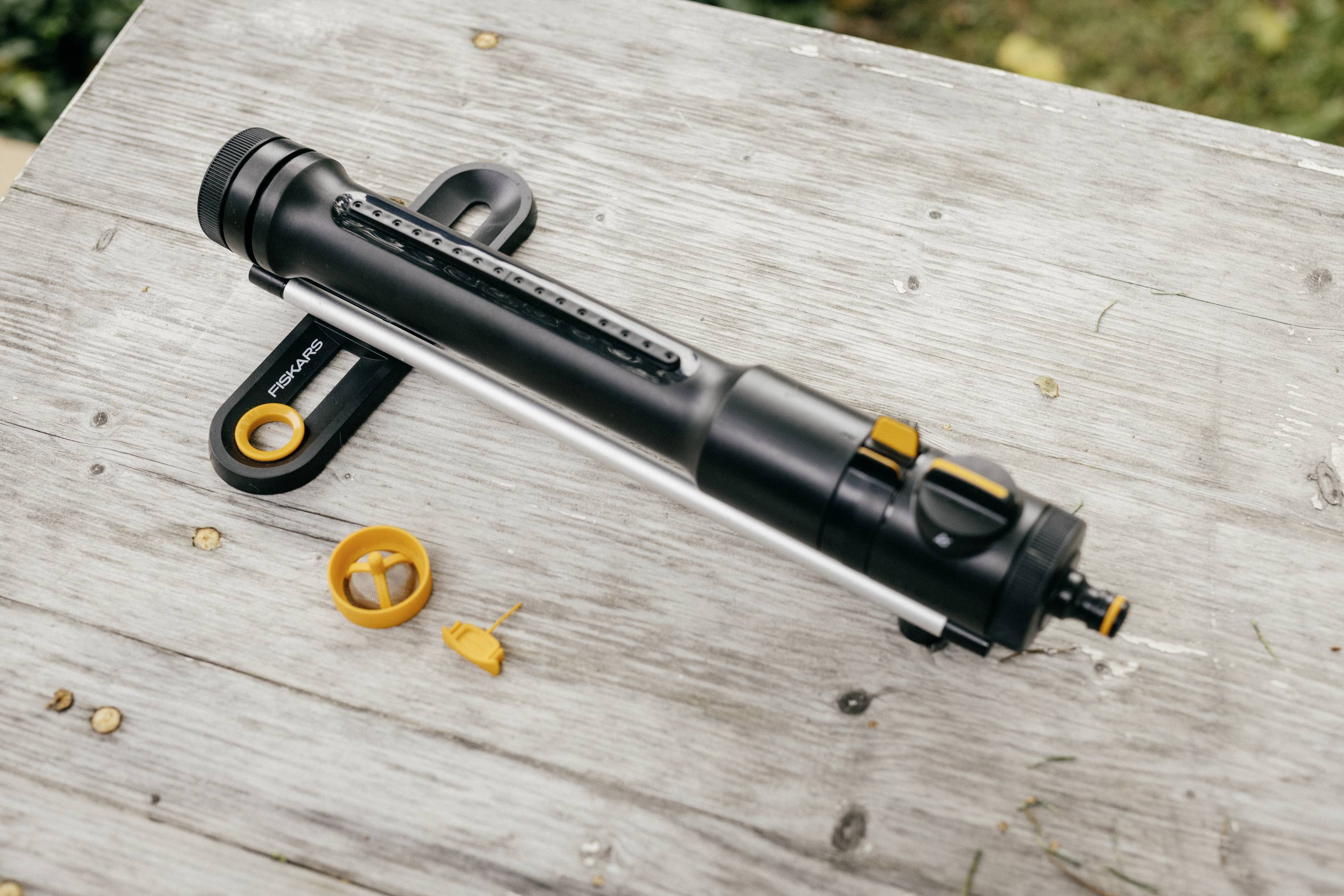 Eine tragbare Luftpumpe mit zwei orangefarbenen Aufsätzen liegt auf einem Holztisch im Freien. Ideal für Fahrräder oder Bälle.