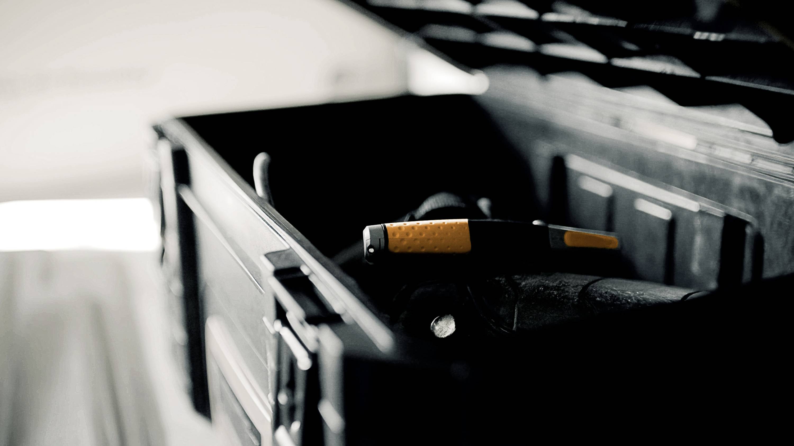 Ein geöffneter Werkzeugkasten mit einem orange-schwarzen Hammer im Vordergrund, in einem leicht beleuchteten Raum.