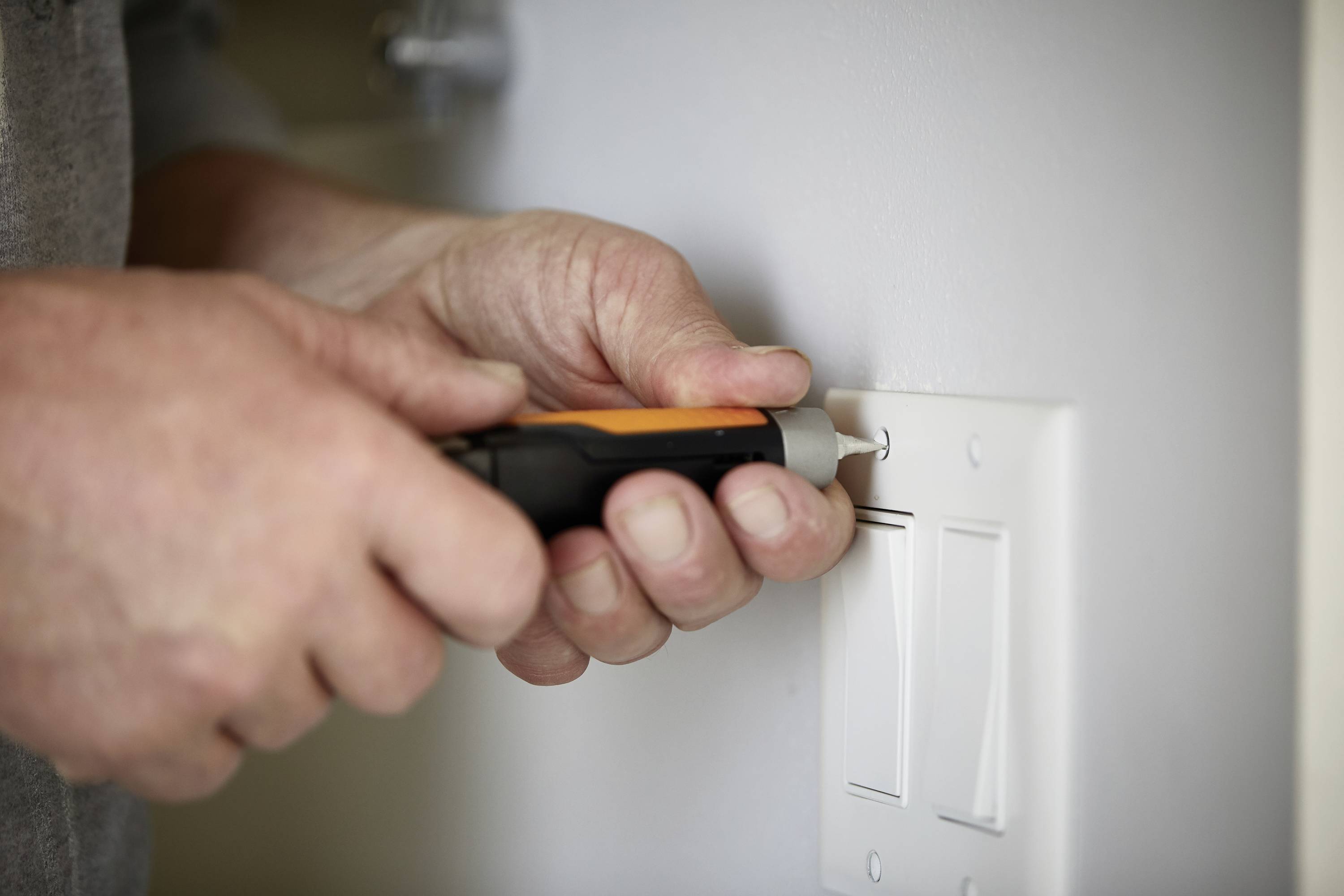 Eine Person installiert oder repariert einen Lichtschalter mit einem Schraubendreher an einer weißen Wand.