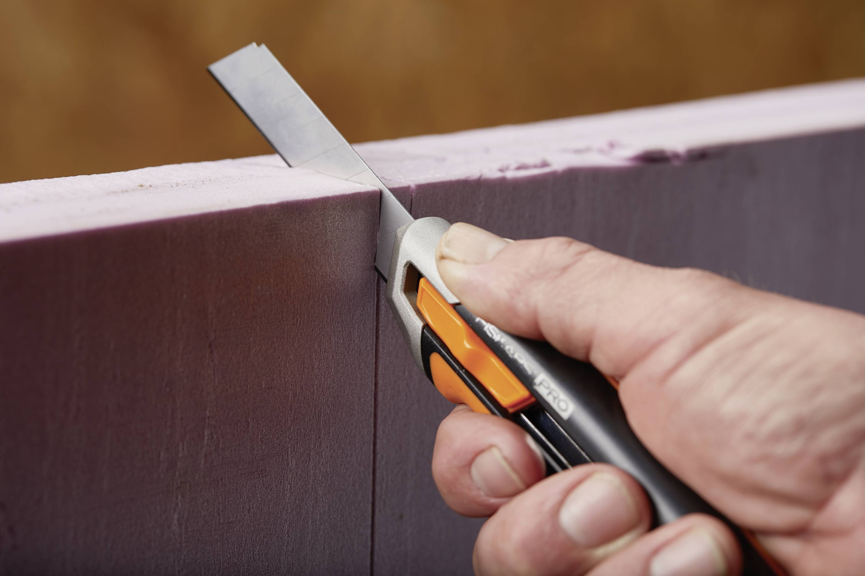 Eine Person schneidet mit einem Cutter-Messer eine rechteckige Platte aus rosa Schaumstoff.