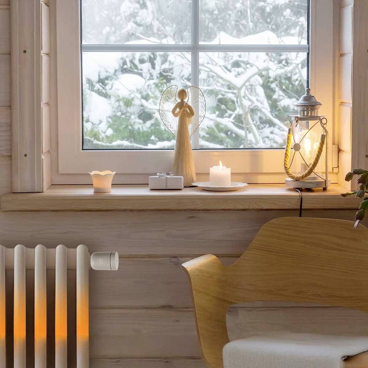 Ein Holzraum mit verschneitem Fenster; auf der Fensterbank stehen ein Engel, Kerzen und eine Laterne. Ein Heizkörper unten links.