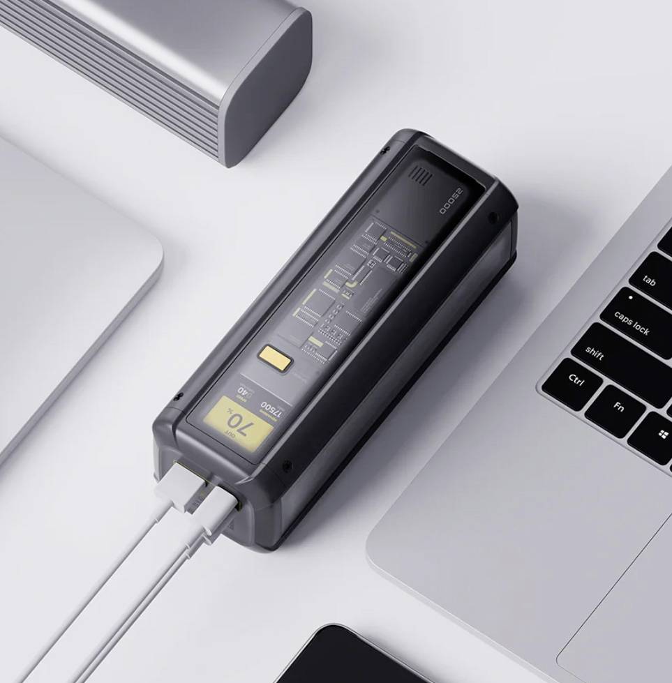 Eine digitale Powerbank, die mit einem Laptop und einem Smartphone verbunden ist und auf ihrem Display 70% Ladung anzeigt, umgeben von anderen elektronischen Geräten.