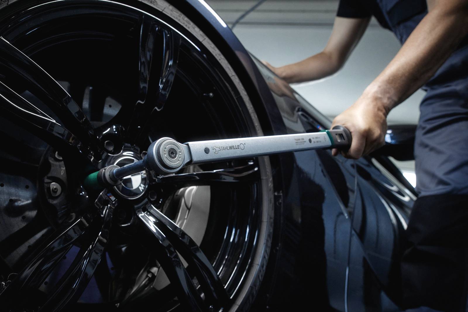 Eine Person zieht mit einem Drehmomentschlüssel die Schrauben eines Autoreifens fest. Der Fokus liegt auf der Werkzeuganwendung.