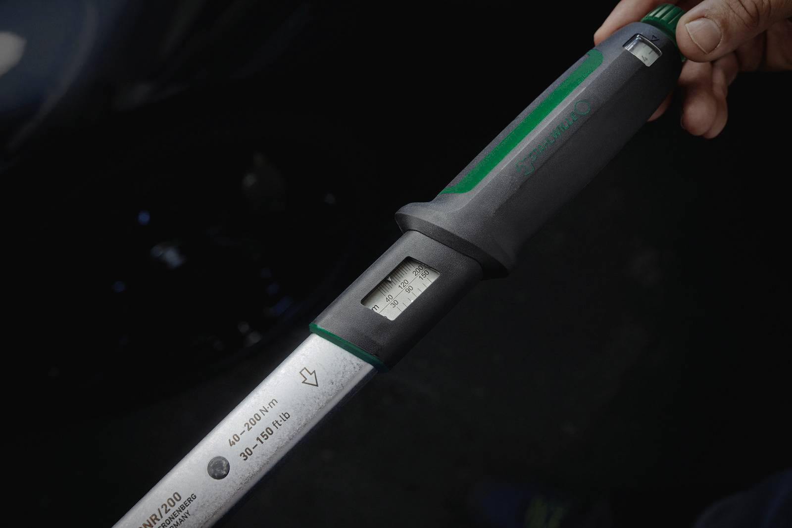 Eine Hand hält einen Drehmomentschlüssel mit digitalem Display, zeigt Skala von 40 bis 200 Nm, Griff mit grünem Akzent.
