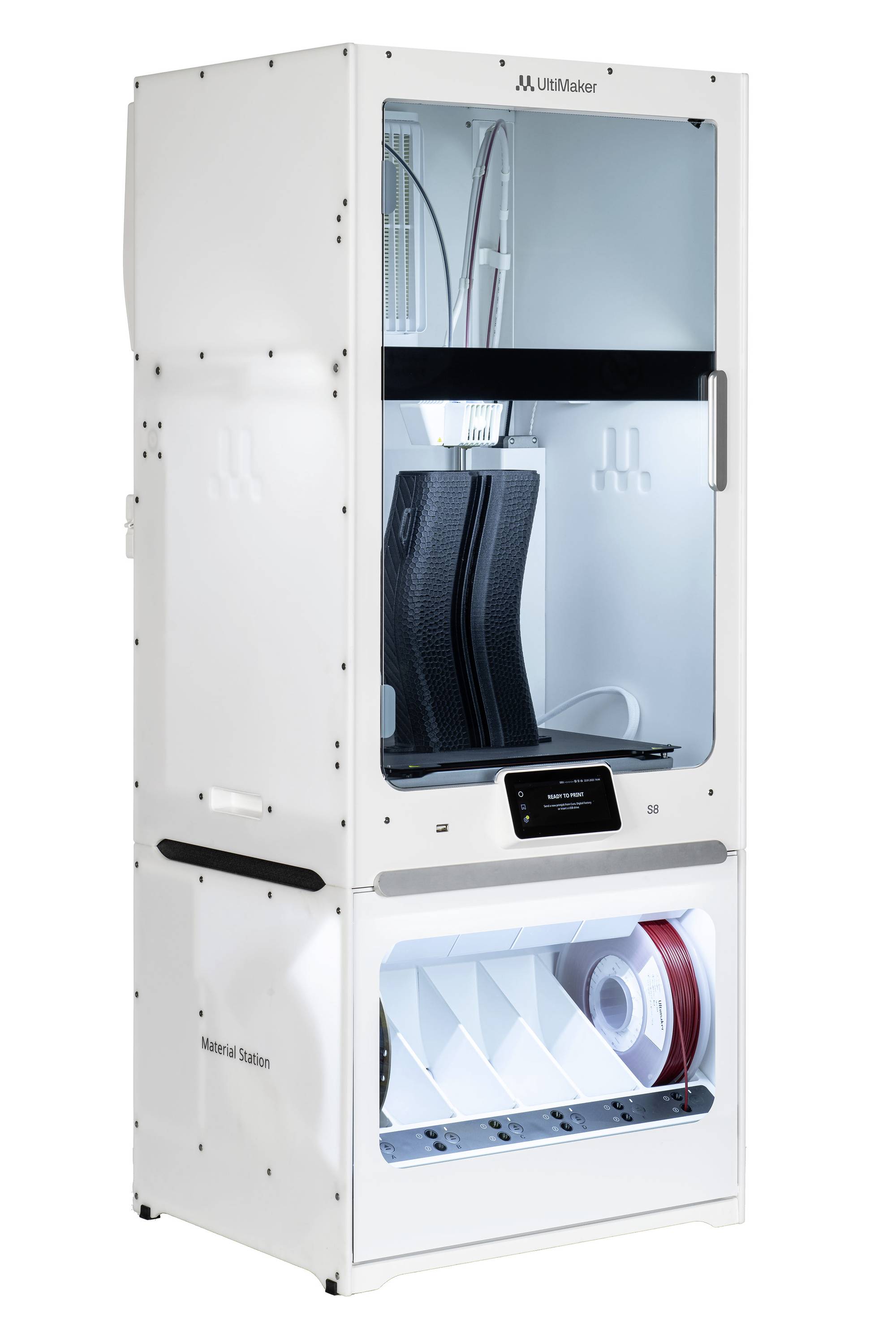 Ein 3D-Drucker mit transparentem Gehäuse zeigt zwei schwarze, halb fertige Objekte. Unten befinden sich Fächer mit Filamentrollen.