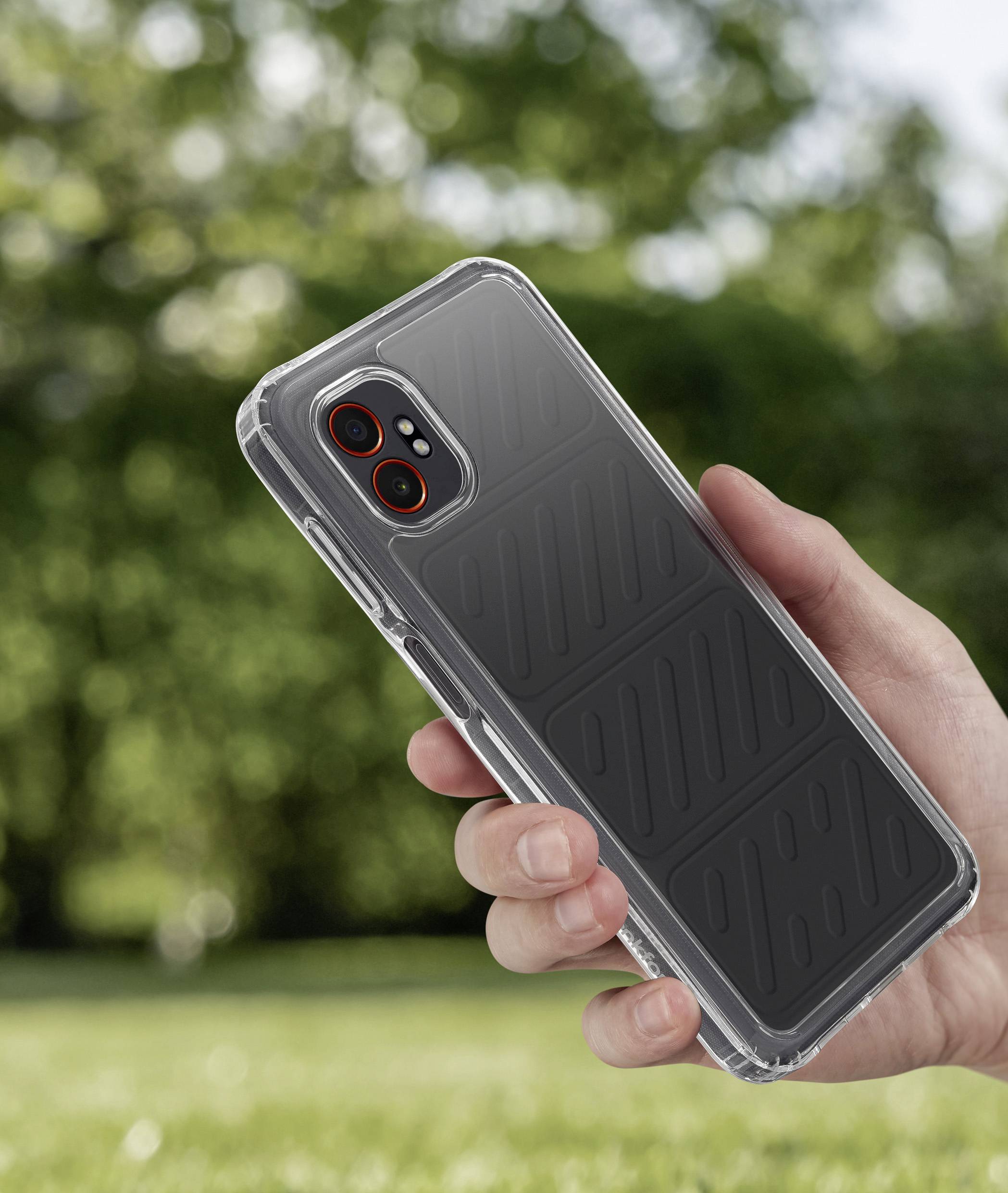 Eine Hand hält ein Smartphone in einem schwarzen Etui im Freien, mit verschwommener Grünpflanzschaft im Hintergrund.