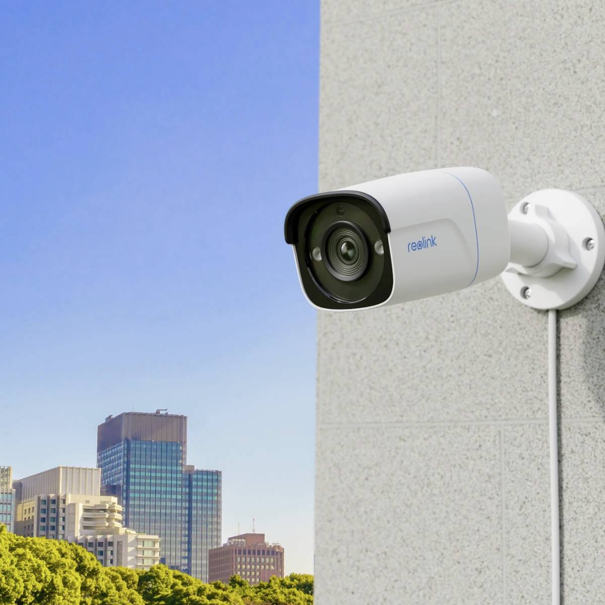 Eine Überwachungskamera ist an der Außenwand eines Gebäudes montiert, mit einer Stadtlandschaft im Hintergrund.