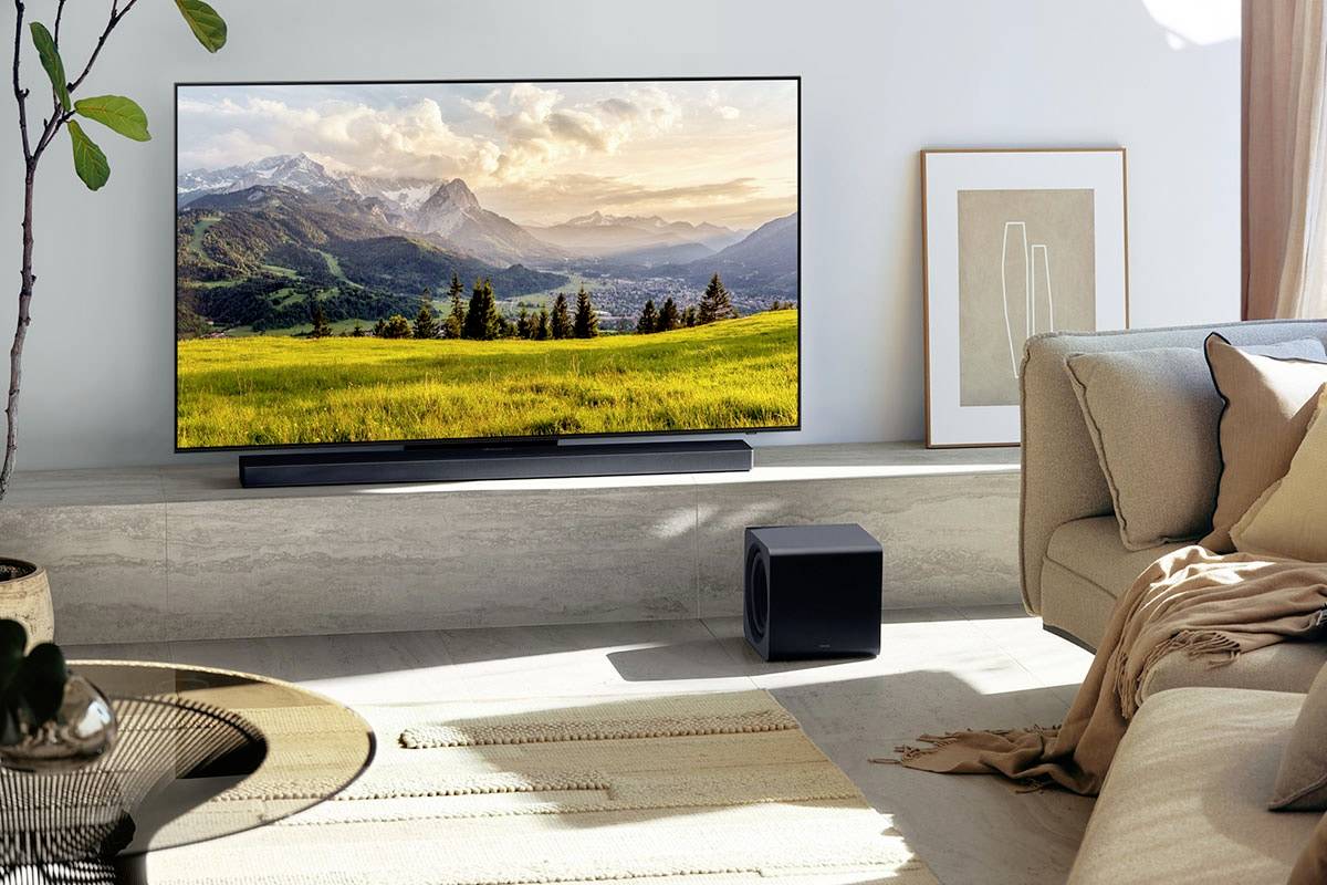 Fernseher in modernem Wohnzimmer zeigt Landschaft mit Bergen und Wiesen. Neutrale Einrichtung mit Sofa und Pflanzen, harmonische Atmosphäre.