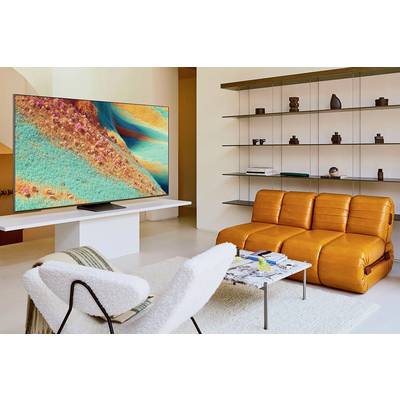 Ein modernes Wohnzimmer mit einem großen, bunten Fernseher an der Wand. Orangefarbene Ledercouch und weiße Stühle im Vordergrund.