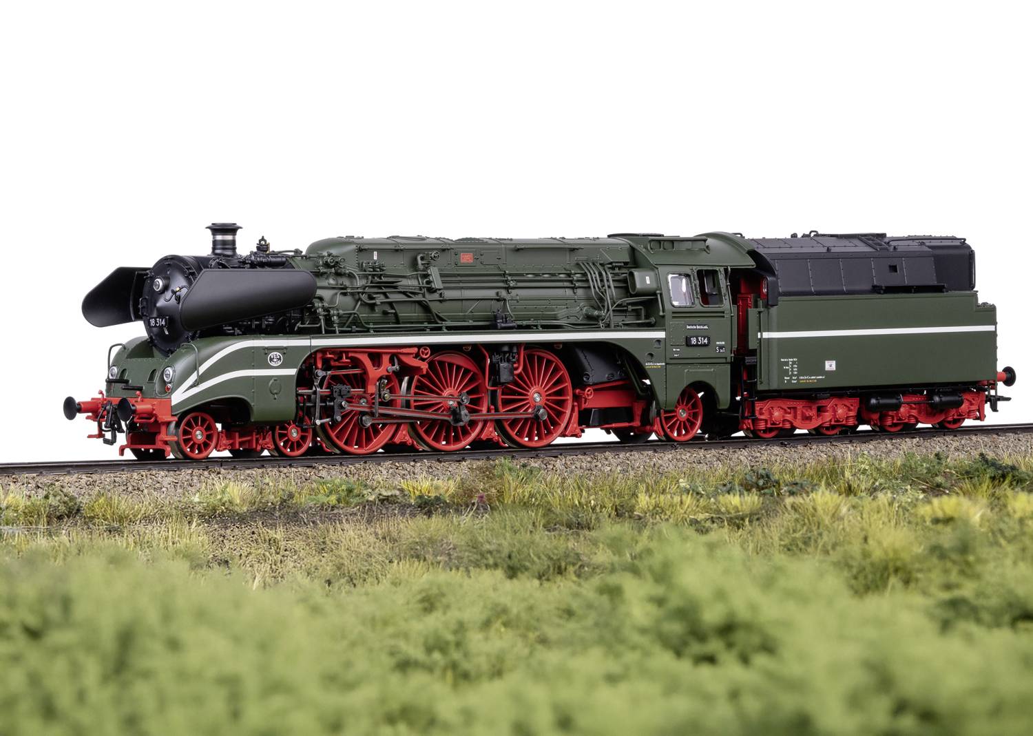 Eine grüne Dampflokomotive mit roten Rädern fährt auf Gleisen über eine Wiese. Sie vermittelt ein nostalgisches Eisenbahngefühl.