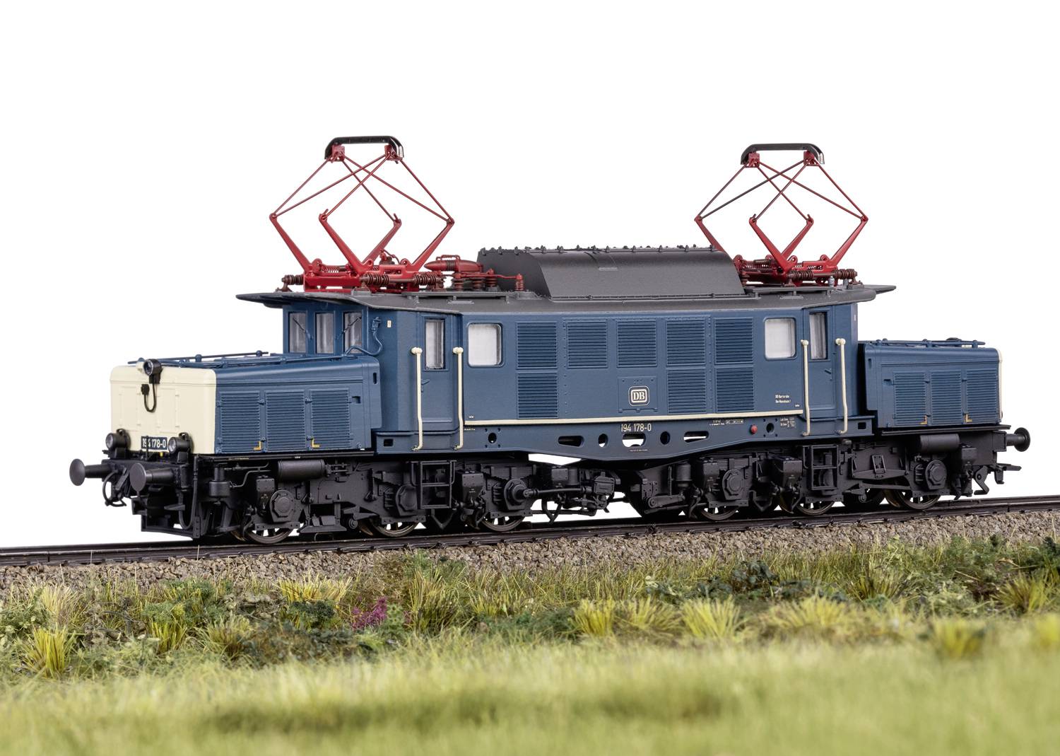 Blaue Modelleisenbahn mit rotem Stromabnehmer fährt auf einem Gleis, grüne Wiese im Vordergrund. Lokomotive der Deutschen Bahn.