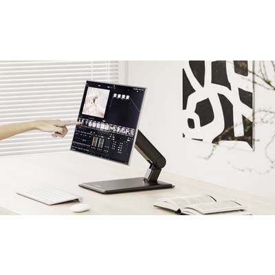 Eine Person bearbeitet ein Video auf einem Computermonitor und zeigt auf den Bildschirm, während eine Tastatur, eine Maus und ein aufgeschlagenes Buch auf dem Schreibtisch liegen.