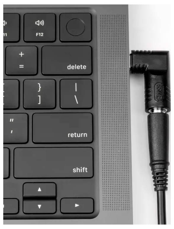 Schwarzes Audiokabel in einen Laptop eingesteckt, neben einer schwarz-grauen Tastatur mit der 'Shift'- und 'Return'-Taste.