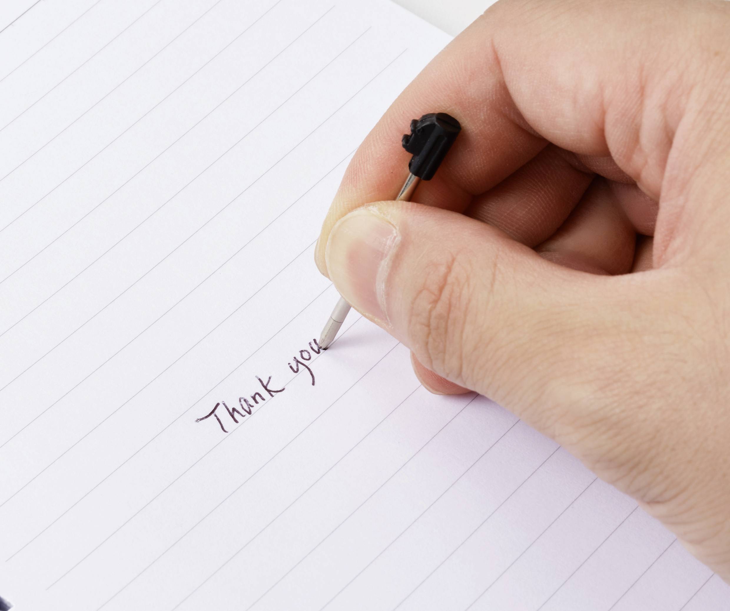 Eine Hand schreibt mit einem Stift auf liniertem Papier die Worte „Danke", und vermittelt dabei Dankbarkeit.