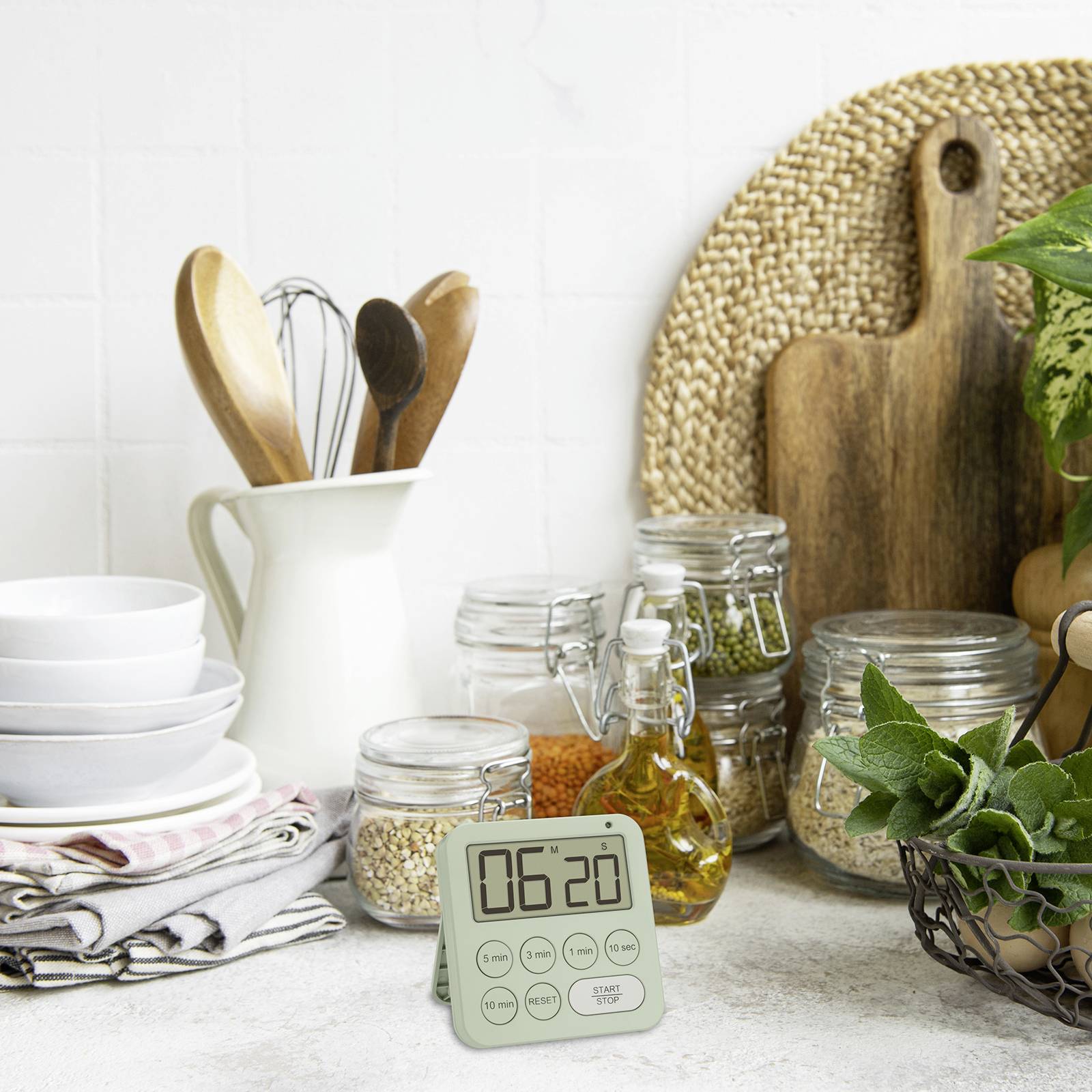 'Küchenszene mit digitalem Timer auf 60:20 Minuten, umgeben von Kochutensilien, Gewürzgläsern und einem Korb mit Kräutern auf heller Arbeitsfläche.'