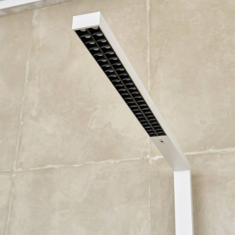 Eine moderne, weiße LED-Schreibtischleuchte mit rechteckigem Kopf und schwarzen Gittern steht vor einer beigen Wand.