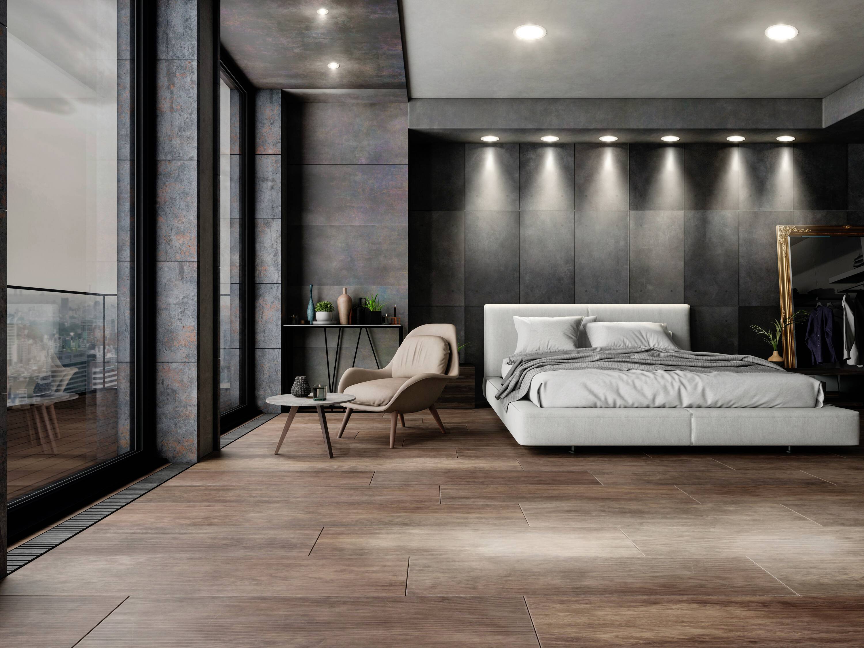 Modernes Schlafzimmer mit grauem Bett, einem Sessel und Tisch. Große Fenster links, bieten Blick nach draußen. Elegant und minimalistisch.