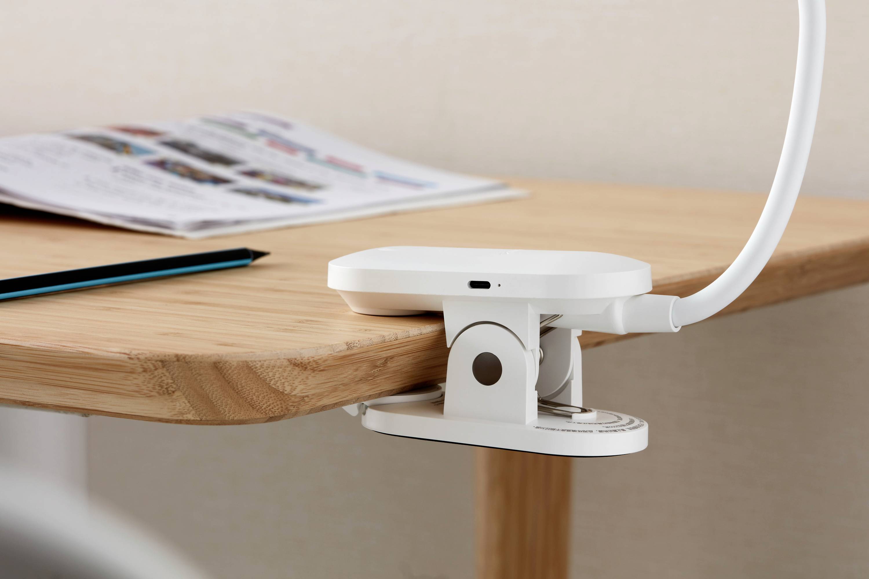 Schreibtisch mit aufgeklebter Leselampe und einem Stift daneben, Reserven eines aufgeschlagenen Magazins dahinter.