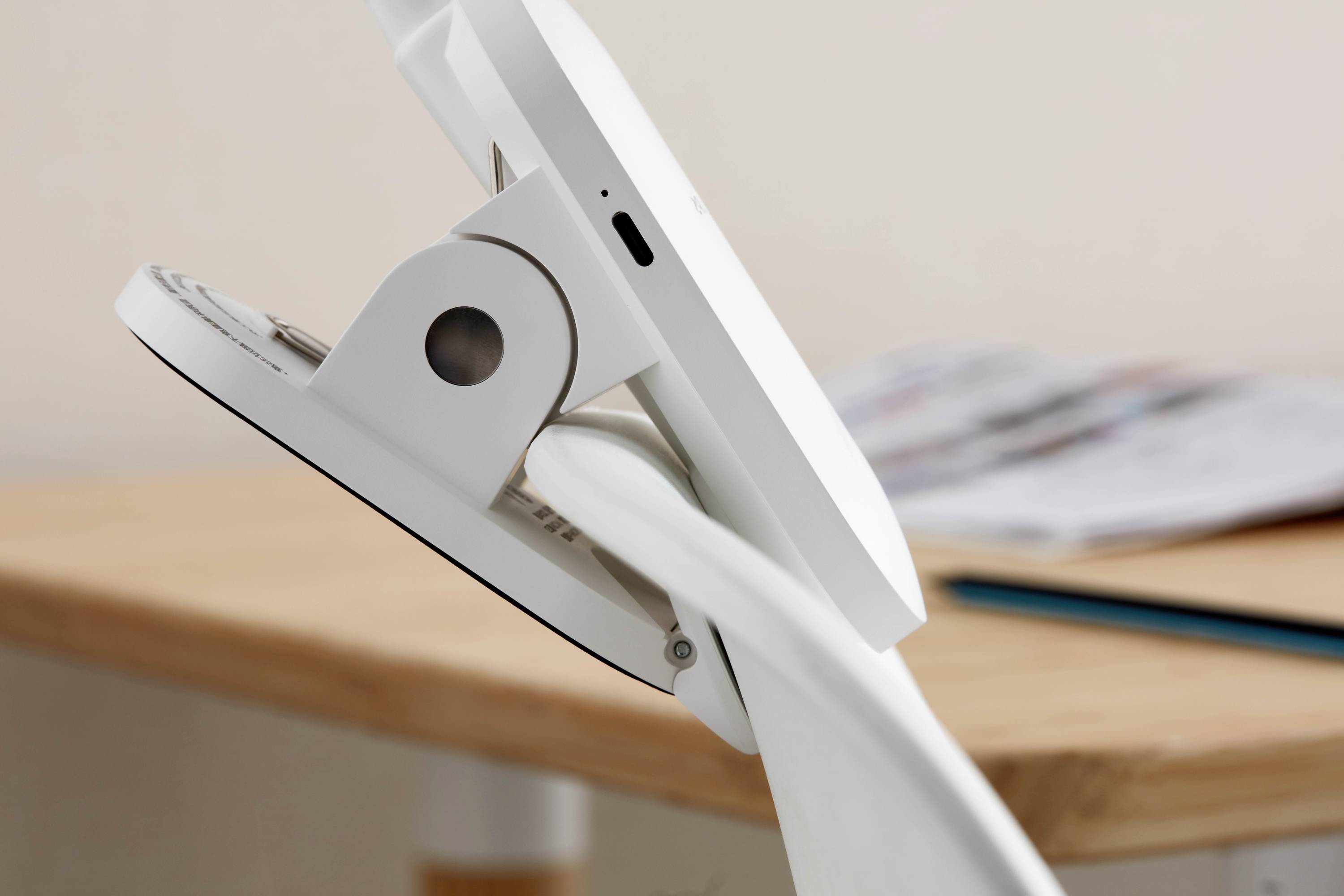 Ein modernes, weißes Tablet auf einem Tisch in einer Halterung neben einer unscharfen Zeitung und einem blauen Stift.