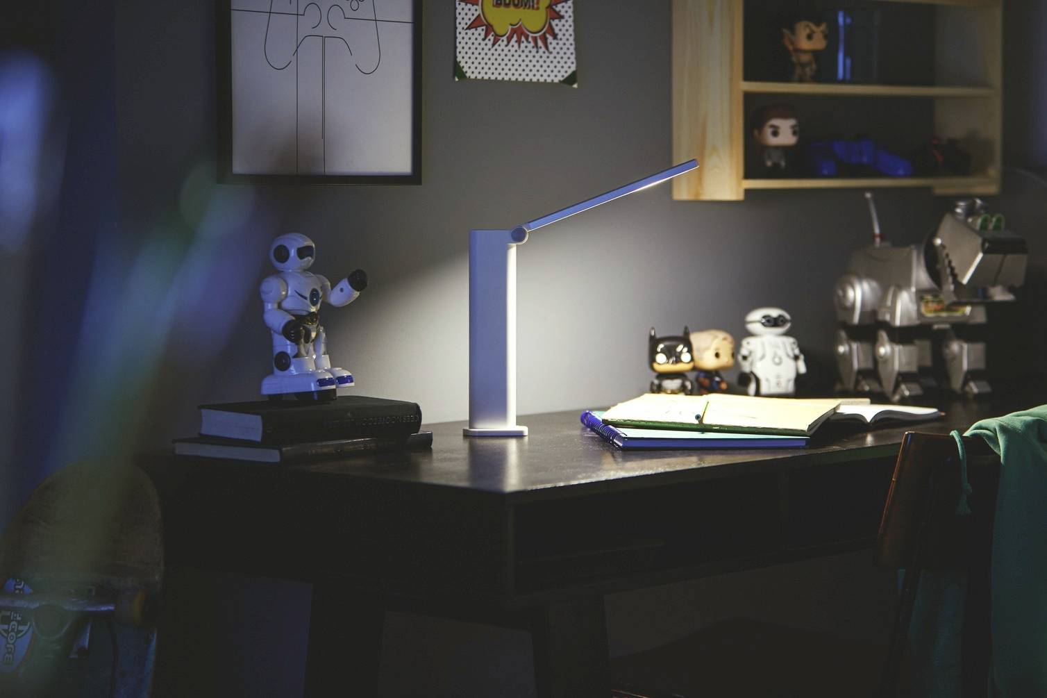 Ein Schreibtisch mit einer Lampe, offenen Büchern und Spielzeugrobotern. Die Szene ist schwach beleuchtet, was eine gemütliche Atmosphäre schafft.