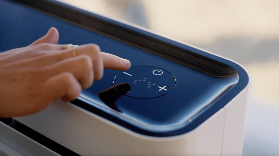 Eine Hand bedient die Touch-Oberfläche eines Geräts mit einem großen Plus- und Minus-Symbol sowie einem Ein-/Ausschalter in der Mitte.