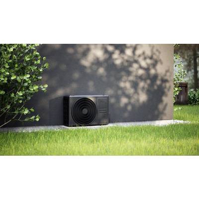 Außenwand eines Hauses mit einer Wärmepumpe. Gerät auf grünem Rasen, umgeben von Pflanzen und Schatten.
