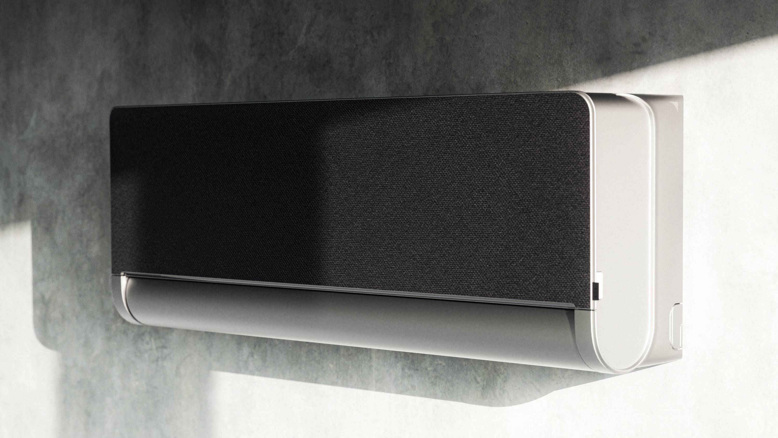 Ein modernes, rechteckiges Klimagerät mit schwarzer Frontabdeckung ist an einer weißen Wand montiert. Sonnenlicht fällt darauf.