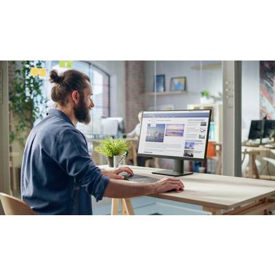 Eine Person mit Bart, die an einem Schreibtisch sitzt, blickt auf einen Desktop-Monitor, der Bilder und Text in einem modernen Büroumfeld zeigt.